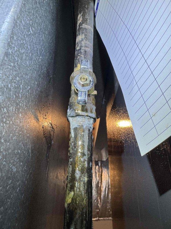 Responded to callback regarding reported gas odor near recently installed air conditioning system. Upon inspection, discovered significant moisture condensation and frost accumulation on refrigerant line connections and fittings. Examined all refrigerant piping joints, brazed connections, and service valves in the installation area. Photographically documented heavy condensation on vertical pipe connections with bolted fittings, as well as ice formation on brass components at insulated line set junction points. Verified system refrigerant integrity and confirmed no refrigerant leaks present at connection points. Determined moisture accumulation was normal condensation due to temperature differential on cold refrigerant lines during system operation. No natural gas lines or combustion equipment present in immediate vicinity of new AC installation. Advised that reported odor was unrelated to air conditioning equipment, as system operates on electricity and sealed refrigerant circuit only