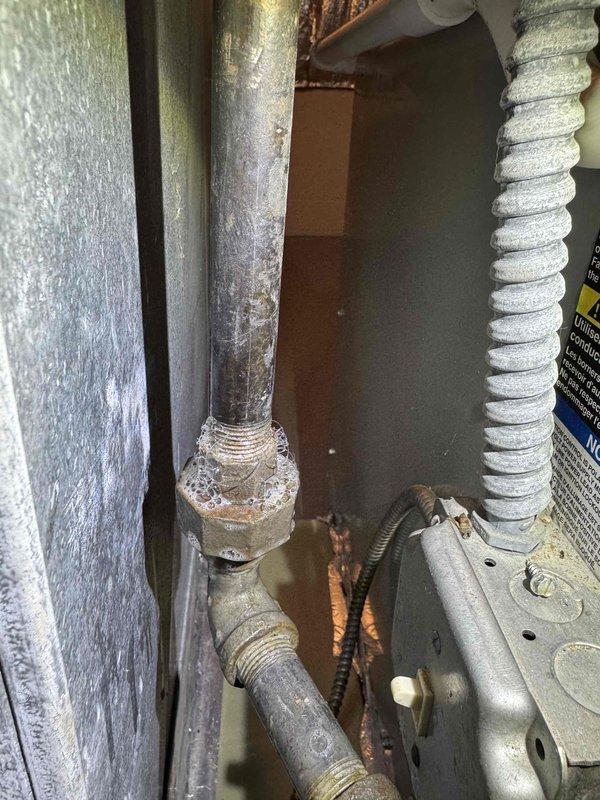 Responded to callback regarding reported gas odor near recently installed air conditioning system. Upon inspection, discovered significant moisture condensation and frost accumulation on refrigerant line connections and fittings. Examined all refrigerant piping joints, brazed connections, and service valves in the installation area. Photographically documented heavy condensation on vertical pipe connections with bolted fittings, as well as ice formation on brass components at insulated line set junction points. Verified system refrigerant integrity and confirmed no refrigerant leaks present at connection points. Determined moisture accumulation was normal condensation due to temperature differential on cold refrigerant lines during system operation. No natural gas lines or combustion equipment present in immediate vicinity of new AC installation. Advised that reported odor was unrelated to air conditioning equipment, as system operates on electricity and sealed refrigerant circuit only