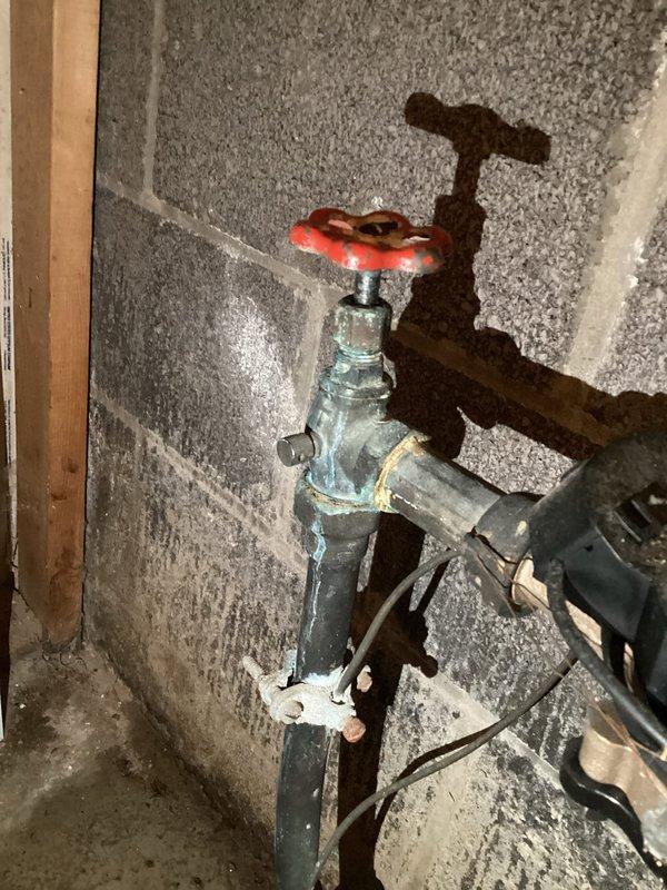 Responded to follow-up complaint regarding persistent moisture in basement utility area following recent pressure valve replacement. Upon inspection, observed significant water staining and white mineral deposits on concrete floor surrounding plumbing installation, indicating ongoing moisture infiltration despite dehumidifier operation. Examined pressure valve assembly mounted on concrete block wall, including red-handled control valve, connecting pipes, and transparent discharge tubing. Assessed water heater connections and associated plumbing components for potential leak sources. Documented floor conditions showing efflorescence patterns and discoloration consistent with continued water exposure. Verified valve installation integrity and investigated drainage system to identify source of persistent dampness in utility space.