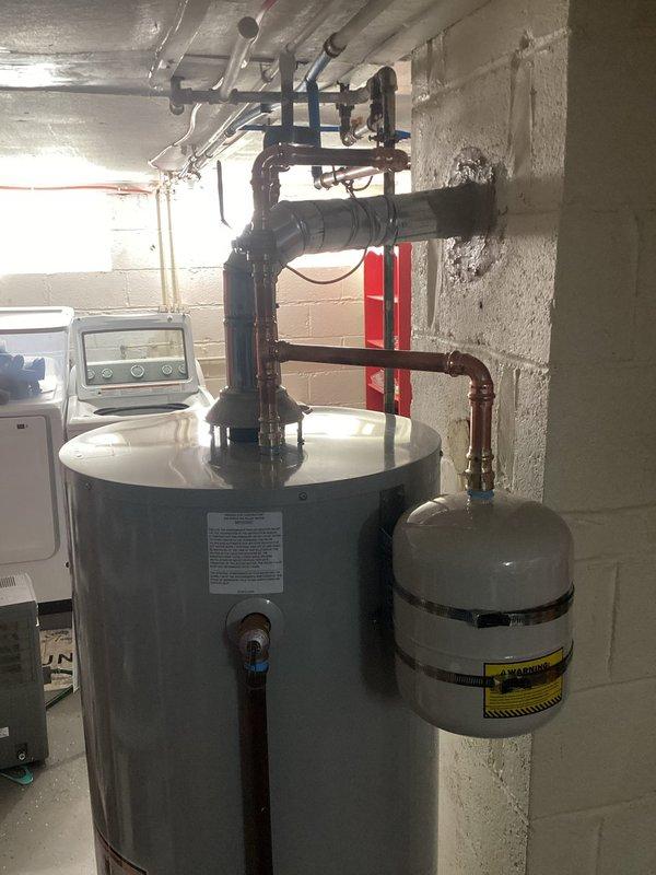 Installed a 50-gallon power vent water heater in basement utility room with all required code upgrades. The installation included proper venting through PVC exhaust system, copper supply line connections, expansion tank mounting with appropriate wall strapping, pressure relief valve installation, and gas line connection with shutoff valve. All plumbing connections were completed using copper piping with proper fittings and soldering, ensuring leak-free operation and compliance with current building codes.