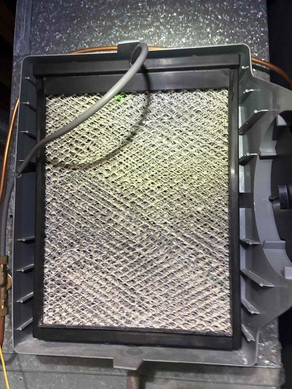 Completed scheduled heating maintenance visit on residential furnace system as part of ongoing preventive maintenance program. Performed comprehensive inspection of air handler unit and evaporator coil assembly. Observed significant dust and debris accumulation on diamond-pattern mesh filter, with visible discoloration transitioning from yellowish-tan to darker gray tones indicating restricted airflow. Inspected refrigerant lines and noted heavy frost and ice buildup on gray foam insulation covering suction line, suggesting potential low refrigerant charge, restricted airflow, or system operating issues. Examined refrigerant line connections and couplings for integrity. Documented conditions of evaporator coil assembly, air handler cabinet, and associated HVAC components through photographic evidence for maintenance records.