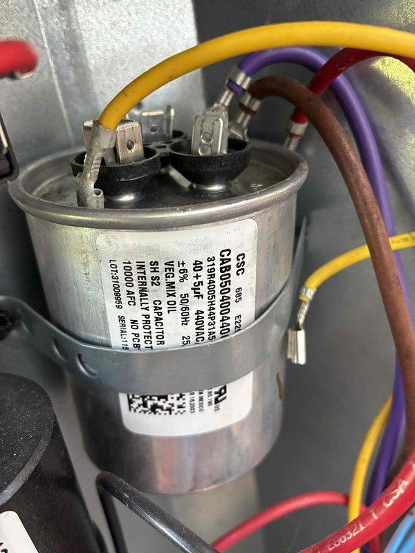 Performed comprehensive HVAC cooling system maintenance on window unit. Conducted electrical diagnostics using clamp meter, measuring amperage draw at 2.93A and voltage at 0.028V to verify proper system operation. Inspected and tested capacitor with connected yellow, purple, and red/brown wiring, confirming secure terminal connections and proper mounting bracket integrity. All electrical components showed normal operation with no signs of damage, corrosion, or unusual wear, and system is functioning within manufacturer specifications.