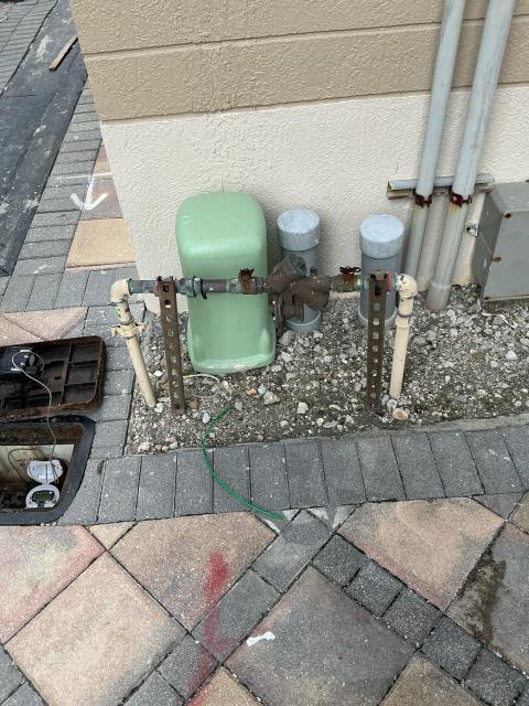Plumbing infrastructure featuring a green backflow preventer and connected pipes in a residential setting, relevant to plumbing services in Boynton Beach, FL.