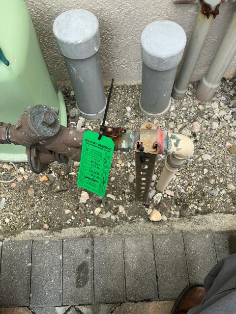 Backflow prevention valve with inspection tag in a residential plumbing setting, showcasing elements relevant to plumbing services in Boynton Beach, FL.