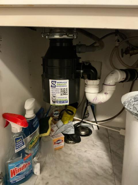 Garbage disposal unit under a kitchen sink with visible plumbing connections and cleaning supplies, representing plumbing services by Service Ready in Boynton Beach, FL.