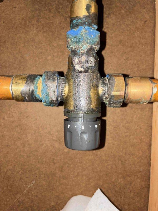 Successfully installed a new mixing valve to replace the heavily corroded existing unit, as observed in the copper pipe junction. The installation required careful connection to the existing plumbing network in the utility area, ensuring proper integration with the comprehensive piping system.