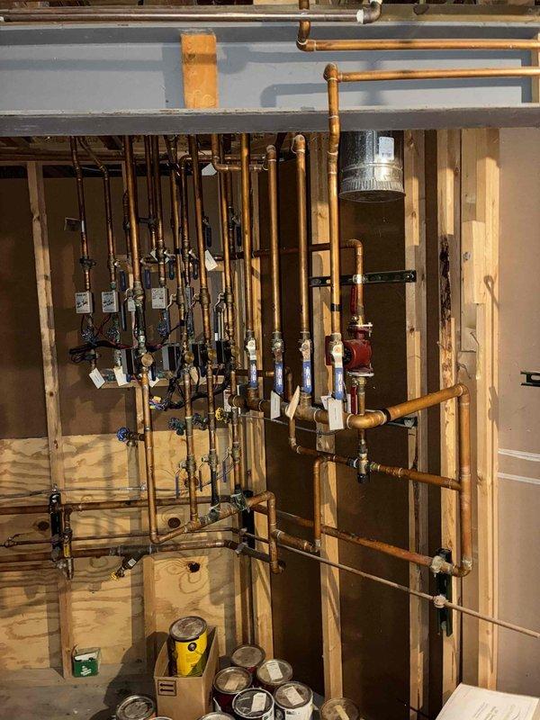 Successfully installed a new mixing valve to replace the heavily corroded existing unit, as observed in the copper pipe junction. The installation required careful connection to the existing plumbing network in the utility area, ensuring proper integration with the comprehensive piping system.