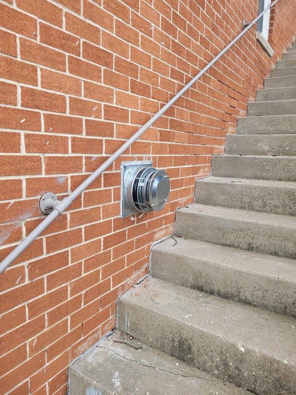 Completed installation of a new wall furnace unit to replace outdated heating system in pine-paneled room. Installed proper exterior ventilation through brick wall with appropriate metal ductwork. Job documentation includes photos of both interior installation and exterior ventilation components.