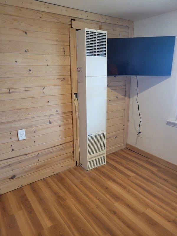 Completed installation of a new wall furnace unit to replace outdated heating system in pine-paneled room. Installed proper exterior ventilation through brick wall with appropriate metal ductwork. Job documentation includes photos of both interior installation and exterior ventilation components.