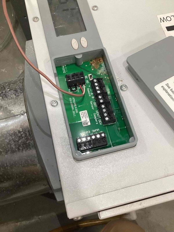 Responded to service call for AA100 control panel malfunction where unit was locked at 40 degrees and customer was unable to adjust setpoint to desired 50 degrees. Upon inspection, discovered corrosion on the green printed circuit board and electronic components within the control panel enclosure. Opened the white metal HVAC control panel to access internal components, revealing compromised relays, terminal blocks, and connection points affected by corrosion. Documented the condition of the circuit board, display screen, control buttons, and wiring connections through photographs. Brought M60 replacement unit to site as directed. Addressed the control malfunction under parts-only warranty coverage. Verified airflow direction labels and inspected all electrical connections and terminal blocks for proper functionality following service intervention.