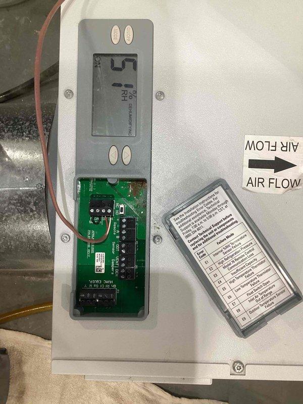 Responded to service call for AA100 control panel malfunction where unit was locked at 40 degrees and customer was unable to adjust setpoint to desired 50 degrees. Upon inspection, discovered corrosion on the green printed circuit board and electronic components within the control panel enclosure. Opened the white metal HVAC control panel to access internal components, revealing compromised relays, terminal blocks, and connection points affected by corrosion. Documented the condition of the circuit board, display screen, control buttons, and wiring connections through photographs. Brought M60 replacement unit to site as directed. Addressed the control malfunction under parts-only warranty coverage. Verified airflow direction labels and inspected all electrical connections and terminal blocks for proper functionality following service intervention.