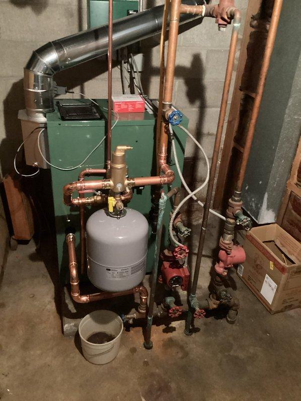 Completed full replacement of 24-year-old residential boiler with new New Yorker boiler system in basement mechanical room. Removed existing unit and installed new green boiler with integrated red display panel, including complete hydronic piping configuration with copper supply and return lines. Installation included white cylindrical expansion tank with brass fittings, multiple red-handled isolation valves throughout system for maintenance access, circulator pump, pressure relief components, and black exhaust flue piping with proper venting. All copper piping, valves, gauges, and connections installed to code specifications. System tested and operational upon completion.