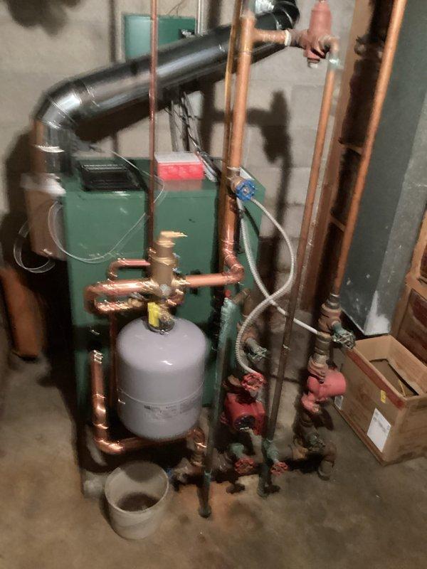 Completed full replacement of 24-year-old residential boiler with new New Yorker boiler system in basement mechanical room. Removed existing unit and installed new green boiler with integrated red display panel, including complete hydronic piping configuration with copper supply and return lines. Installation included white cylindrical expansion tank with brass fittings, multiple red-handled isolation valves throughout system for maintenance access, circulator pump, pressure relief components, and black exhaust flue piping with proper venting. All copper piping, valves, gauges, and connections installed to code specifications. System tested and operational upon completion.
