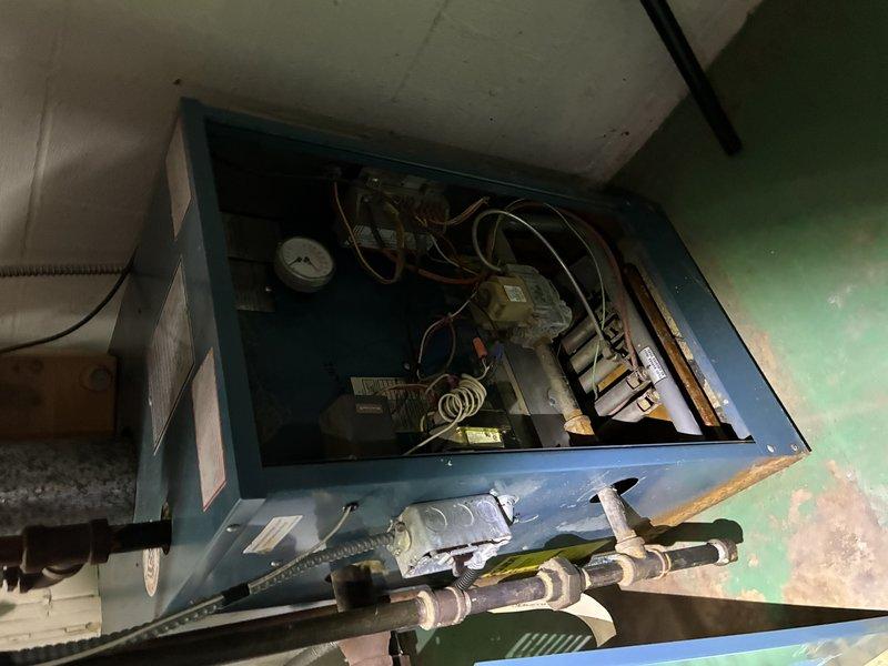Performed post-flooding inspection on boiler and furnace system. Upon arrival, found extensive water damage with significant debris accumulation, including fibrous material buildup throughout mechanical components and visible corrosion on piping and connections. Inspected boiler cabinet, pressure gauge, valve assemblies, and associated piping for water damage and operational integrity. Documented equipment condition with photos showing rust formation on threaded connections, paint deterioration on cabinet surfaces, and potential contamination around pipe entry points. System components showed signs of extended service without recent maintenance, compounded by flood-related debris and moisture exposure.