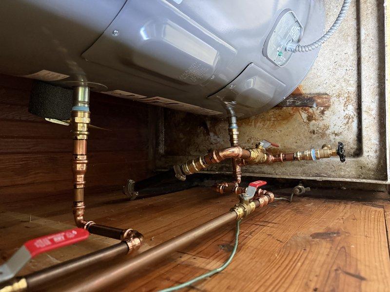 Completed installation of a 30-gallon Rheem electric water heater in a residential utility space. Removed existing unit and installed new water heater on wooden platform, connecting copper supply lines with brass ball valves and fittings. Installed flexible metallic conduit for electrical connection, verified all plumbing connections for proper seal and operation, and ensured compliance with manufacturer specifications and local code requirements.