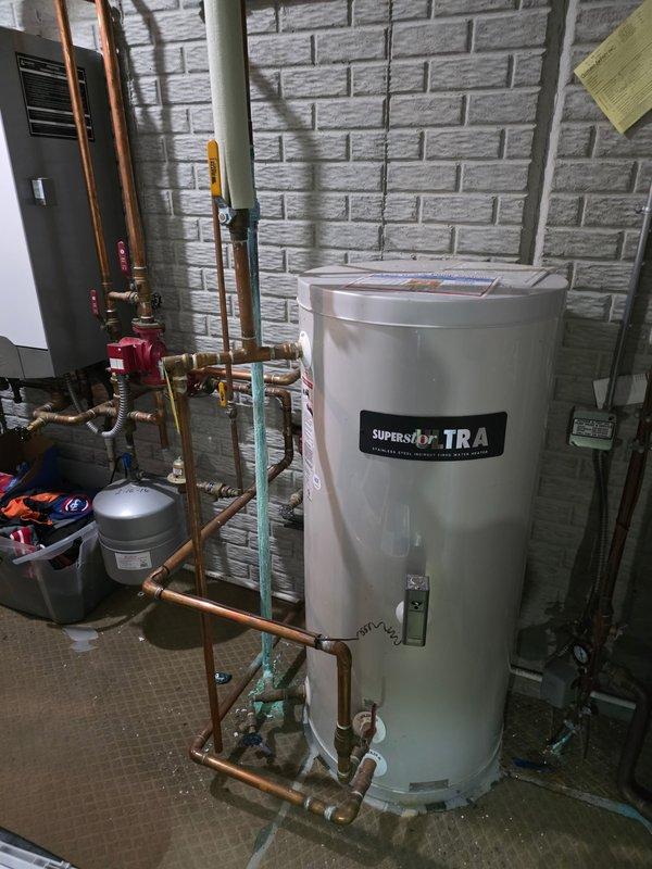 Responded to emergency service call for leaking copper pipe with severe corrosion. Upon arrival, found vertical copper cold water supply line completely covered in thick turquoise-green corrosion and actively leaking. Replaced deteriorated copper piping connected to water heater system. Installation included new copper pipe, brass fittings, and proper connections to existing SuperStor water heater and associated plumbing components including circulator pump and expansion tank.