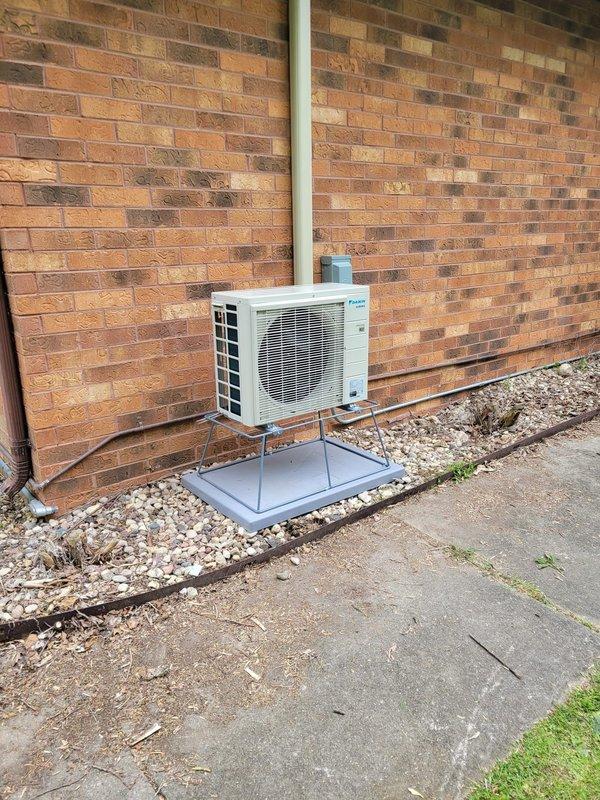 Completed installation of Daikin mini split heat pump system with indoor unit mounted in master bedroom and outdoor condensing unit positioned on exterior brick wall directly opposite. Utilized existing abandoned 3/4" conduit from previous pool sub panel for electrical connection, installed disconnect box on exterior wall, and secured refrigerant line set vertically along brick facade. Outdoor unit mounted on elevated platform with proper clearances over gravel base, system tested and operational.