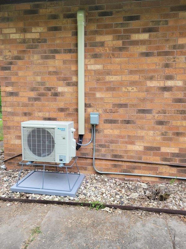 Completed installation of Daikin mini split heat pump system with indoor unit mounted in master bedroom and outdoor condensing unit positioned on exterior brick wall directly opposite. Utilized existing abandoned 3/4" conduit from previous pool sub panel for electrical connection, installed disconnect box on exterior wall, and secured refrigerant line set vertically along brick facade. Outdoor unit mounted on elevated platform with proper clearances over gravel base, system tested and operational.