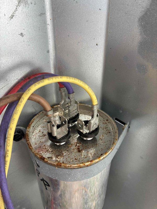 Responded to no cooling complaint on aging residential HVAC system. Upon inspection, found outdoor condensing unit running but not providing cooling to structure. Diagnosed failed dual run capacitor evidenced by severe corrosion and rust on terminal plate, preventing compressor from operating properly. Replaced defective capacitor with manufacturer-specified component, verified proper electrical connections, and tested system operation. Unit restored to normal cooling function with compressor and condenser fan motor running within specifications.