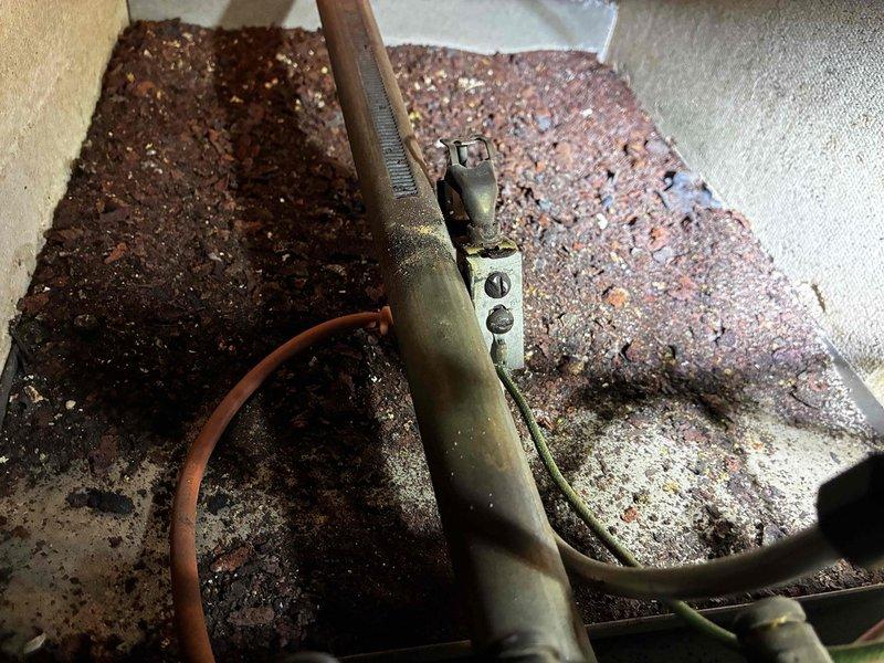 Performed comprehensive boiler tune-up and inspection on residential heating system in preparation for property sale. Upon arrival, assessed unit condition and determined system was suitable for maintenance service. Conducted thorough cleaning of heat exchanger coils which exhibited heavy accumulation of dust and debris between cooling fins. Inspected boiler components including burner assembly, heat exchanger surfaces, and associated piping connections. Documented system condition with photographic evidence showing corroded floor-mounted piping channels and contaminated coil surfaces requiring attention. Unit was operational at time of service but showed signs of age and deferred maintenance throughout accessible components.