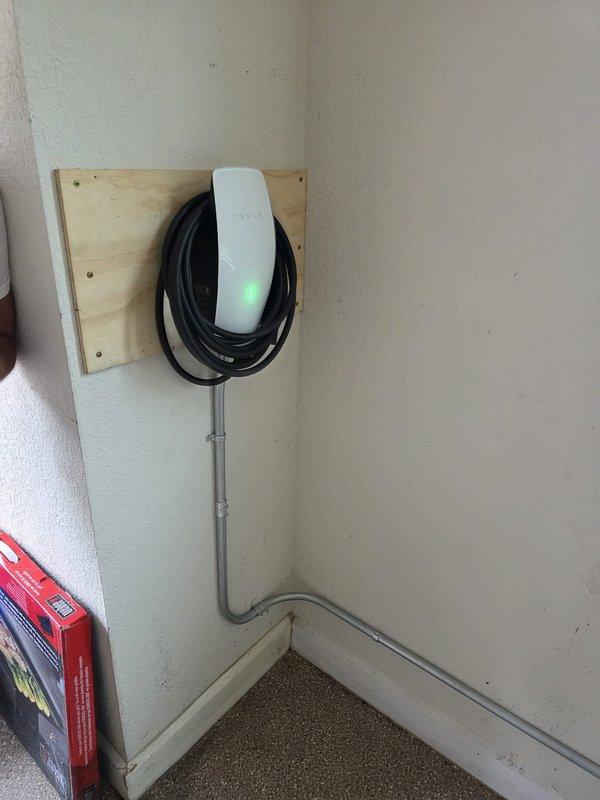 Relocated existing EV charger to right side of room and modified existing 3/4" conduit system by cutting and lowering the pipe run. Installed wood backing plate for secure mounting of customer-supplied Tesla wall charger. Extended conduit approximately 35 feet from existing junction box on left side of room to new charger location, running along wall and baseboard. Completed installation with proper mounting, electrical connections, and conduit terminations for fully operational Tesla charging station.