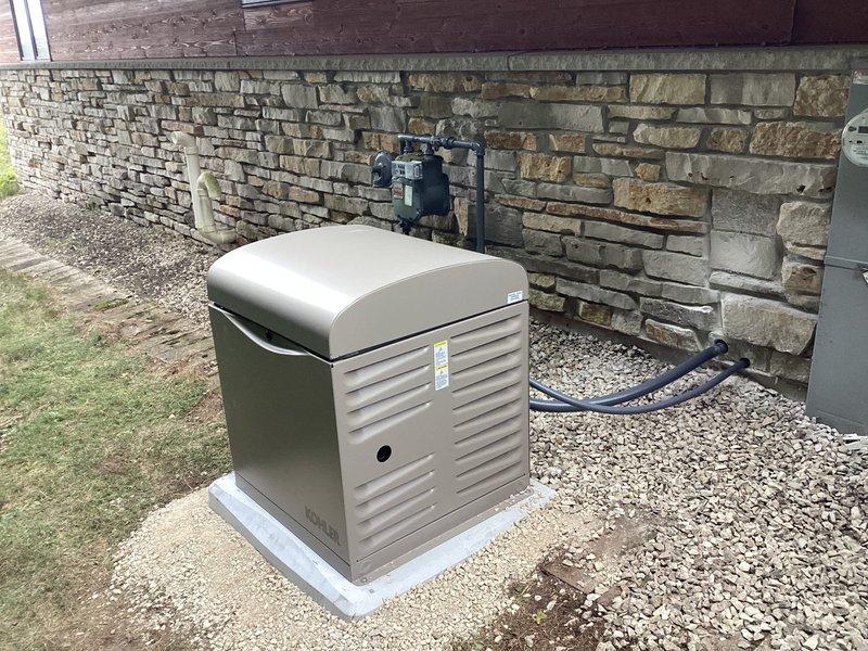 Installed Kohler 12RESV 12KW air-cooled home standby generator with steel cabinet on concrete pad adjacent to existing AC unit on side of residence. Mounted 100-amp, 16-space automatic transfer switch next to main electrical panel to provide backup power to owner-selected circuits during outages. Completed all line voltage and low-voltage wiring connections between generator, transfer switch, and electrical panel per manufacturer specifications. Installed battery and carburetor heater for cold weather operation.

Relocated three small evergreen shrubs from installation area to accommodate generator placement. Ran natural gas supply line from existing gas meter to generator, including all necessary pipe, fittings, and connections for fuel supply. Painted exterior gas piping gray using oil-based paint for corrosion protection and aesthetic finish. Verified proper gas pressure and flow to unit.

Tested automatic transfer switch operation and confirmed seamless transition between utility a