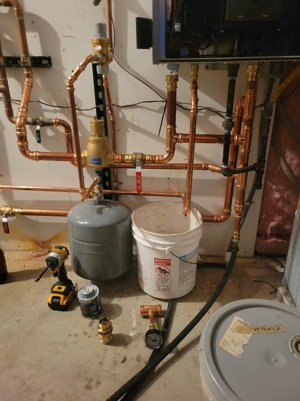 Completed Day 1 of boiler replacement installation, removing existing outdated unit and beginning installation of new boiler system. Installed complex copper piping network with multiple vertical and horizontal runs, incorporating brass mixing valves, expansion tank, and necessary fittings and connections. New boiler control panel programmed and operational, displaying system parameters including outlet temperature of 158°F with target setpoint of 173°F, operating at 99% power output and 6.0 psi system pressure in single boiler configuration mode with domestic hot water demand settings enabled.