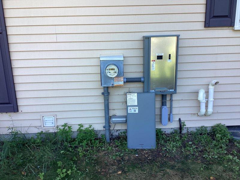 Installed Kohler model 26RCA 26kW air-cooled standby generator with aluminum cabinet on compacted gravel with concrete base at side of residence. Mounted 200A service-rated automatic transfer switch adjacent to electrical meter socket and relocated existing PVC exhaust piping to accommodate installation. Separated grounds and neutrals in existing main electrical panel, provided proper grounding and bonding per code requirements. Installed battery, carburetor heater, and oil heater with generator unit. Ran necessary low-voltage and line-voltage wiring from generator to transfer switch and main panel. Installed natural gas piping and fittings from existing gas line to generator, painting exterior gas line gray with oil-based paint. Verified all electrical connections, tested automatic transfer switch operation, and confirmed proper generator startup and load transfer functionality.