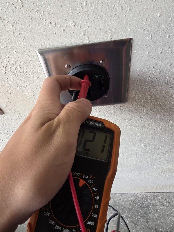 Landed the main feeder conductors on the panel lugs and installed a 2-pole, 30-amp breaker in the available main breaker space, then installed a 30-amp receptacle beneath the panel. Verified the circuit with a digital multimeter, measuring approximately 121 VAC at the receptacle, confirming proper voltage and operation. Receptacle is mounted in a stainless steel cover plate and secured with screws.
