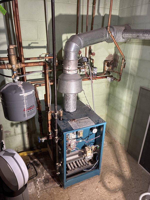 Performed a pre-winter inspection of the gas-fired hydronic boiler system in response to reported inadequate heating and a slow leak. Found the original 2014 Amtrol expansion tank leaking at the top fitting, with heavy corrosion and mineral buildup on the tank and surrounding copper piping and fittings, and noted water staining at the base of the boiler. Documented conditions with photos; the expansion tank and other components require replacement, and a repair quote is being prepared.
