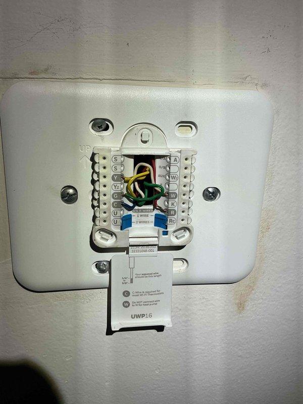 Responded to after-hours call for thermostat issue on a 5-year-old HVAC system. Inspected the thermostat wiring connections at the wall plate (UWP16), verifying proper terminal connections for the yellow, green, white, and red wires. Also examined the system ductwork and refrigerant line set, noting the condition of the galvanized metal components and insulated copper piping.