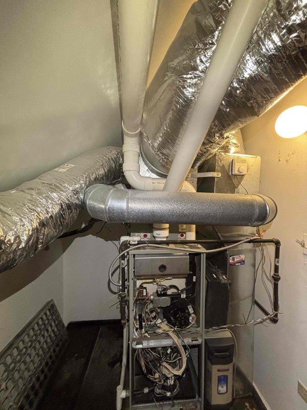 Responded to commercial HVAC water leak service call for a 6-year-old system. Diagnosed water accumulation from condensate drain line blockage in utility area, cleared obstruction in PVC drainage pipes, and verified proper system operation. Documented repair with photos showing furnace unit with exposed control panel and the drainage configuration after service completion.