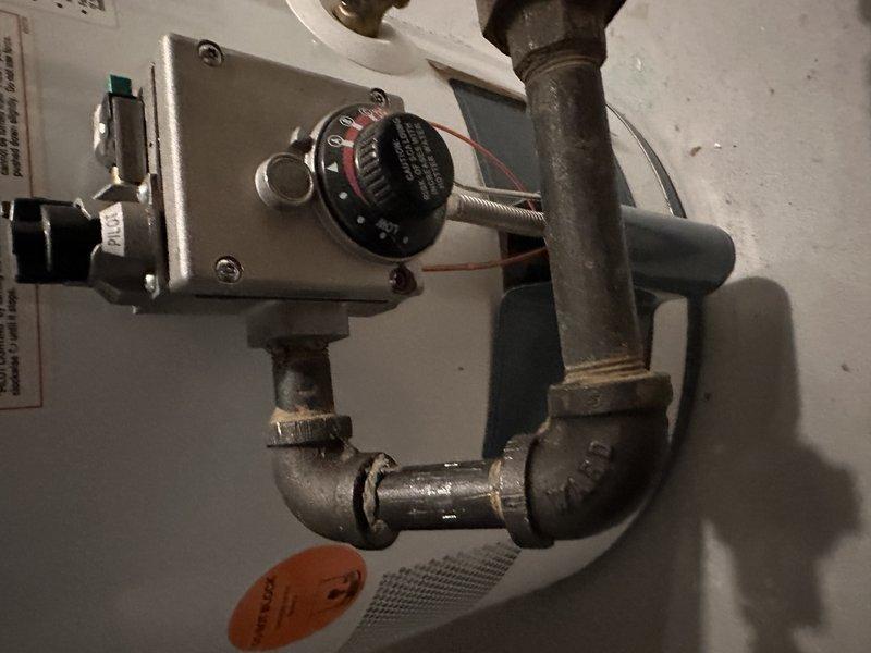 Performed inspection of existing water heater system for family friend referral. Examined control valve assembly on water heater tank, noting condition of temperature regulation dial and connected metal piping configuration. Documented current installation including copper supply lines, gas valve, and associated ductwork to determine replacement options and provide appropriate recommendations for system upgrade.