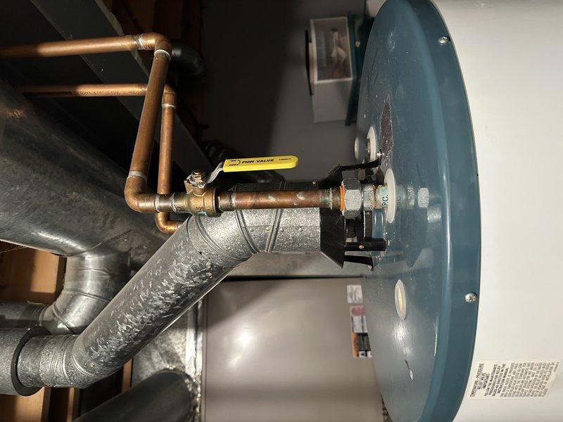 Performed inspection of existing water heater system for family friend referral. Examined control valve assembly on water heater tank, noting condition of temperature regulation dial and connected metal piping configuration. Documented current installation including copper supply lines, gas valve, and associated ductwork to determine replacement options and provide appropriate recommendations for system upgrade.