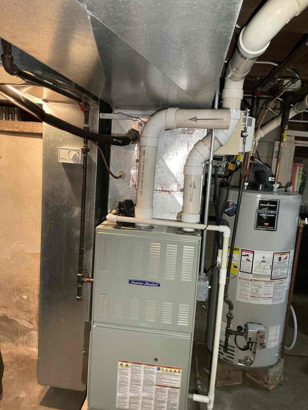Responded to service call for humidifier noise issue on 15-year-old unit. Inspected American Standard furnace system with attached humidifier mounted in beige frame. Evaluated complete HVAC setup including connected PVC ventilation pipes, water lines, and electrical connections to resolve the reported noise concern.