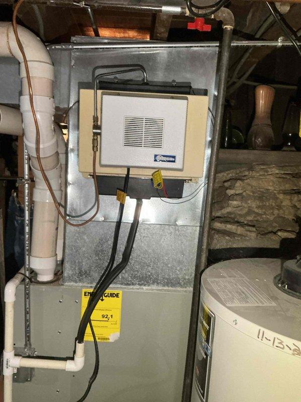 Responded to service call for humidifier noise issue on 15-year-old unit. Inspected American Standard furnace system with attached humidifier mounted in beige frame. Evaluated complete HVAC setup including connected PVC ventilation pipes, water lines, and electrical connections to resolve the reported noise concern.