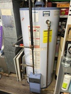 Conducted comprehensive assessment of 20+ year old Kenmore water heater requiring replacement. Unit shows significant age deterioration with installation date noted as "10-20-07" and is located in confined utility space with existing galvanized metal ductwork and copper supply lines. Provided customer with detailed replacement options and cost estimate for complete system upgrade.