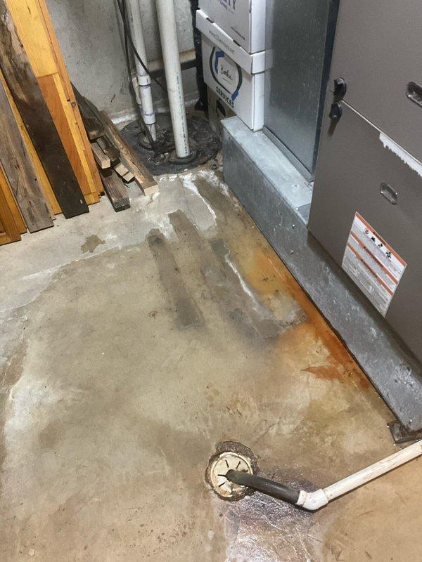 Upon inspection of the 15-year-old furnace, identified water leakage issues evidenced by significant staining and moisture damage on the concrete floor surrounding the unit. Evaluated the drainage system, noting mineral deposits and sediment buildup around the floor drain, and confirmed proper connection of the PVC condensate line to the drainage system.