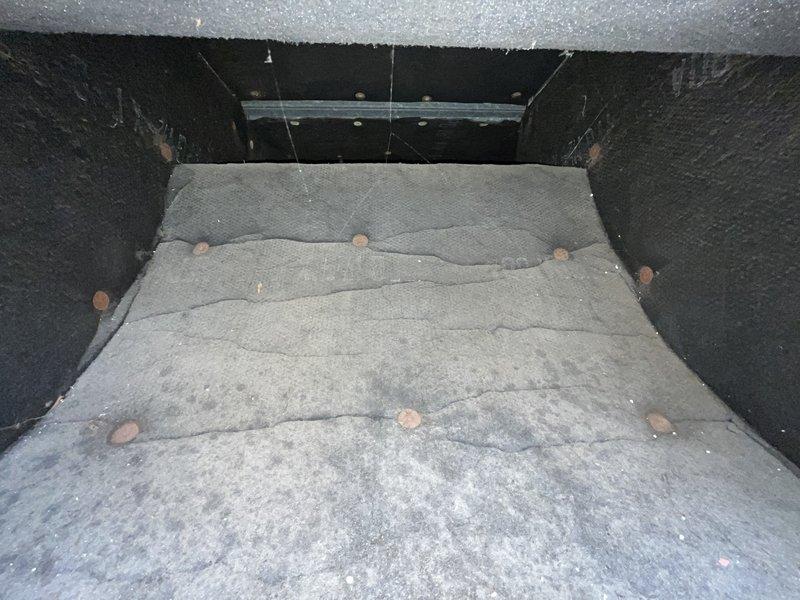 Performed site assessment of rooftop commercial air conditioning system to provide replacement estimate for condenser and evaporator coil. Accessed rooftop mechanical equipment through concrete-lined compartment with weathered access panel showing signs of age and corrosion. Inspected ductwork plenum and air handling components, noting fibrous insulation material with visible wear patterns and multiple mounting fasteners. Documented existing system configuration including galvanized metal panels and insulation conditions within the compartment. Photographed equipment access points and internal ductwork components to support estimate preparation for complete condenser and coil replacement on commercial HVAC system.