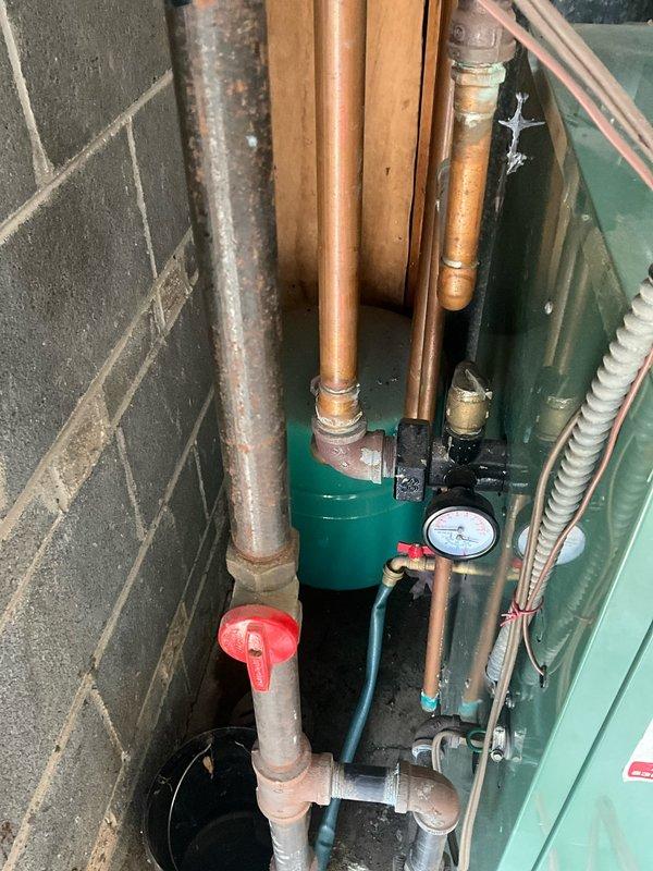 Responded to service call for reported boiler leak. Upon arrival, performed comprehensive inspection of New Yorker boiler system and associated plumbing components. Examined copper piping network showing signs of age-related corrosion and oxidation, teal expansion tank, pressure gauge, and various valves throughout the mechanical system. Identified source of leak in plumbing assembly and assessed overall system condition. Utilized pipe wrenches and hand tools to address the leak issue and tighten connections as needed to restore proper system operation.