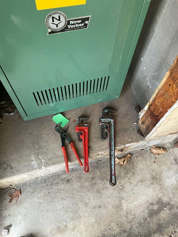 Responded to service call for reported boiler leak. Upon arrival, performed comprehensive inspection of New Yorker boiler system and associated plumbing components. Examined copper piping network showing signs of age-related corrosion and oxidation, teal expansion tank, pressure gauge, and various valves throughout the mechanical system. Identified source of leak in plumbing assembly and assessed overall system condition. Utilized pipe wrenches and hand tools to address the leak issue and tighten connections as needed to restore proper system operation.