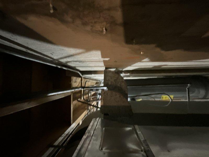 Conducted on-site assessment for ductwork removal required to facilitate wall repair due to active water leak. Evaluated existing HVAC system configuration in confined ceiling cavity, including horizontal metal supply duct with insulated branch runs secured to structural framing. Documented water-damaged ceiling areas showing brown staining and deterioration near ductwork penetrations. Provided estimate for temporary ductwork disconnection and removal to allow access for plumbing repairs and structural wall support, with subsequent reinstallation upon completion of remediation work.