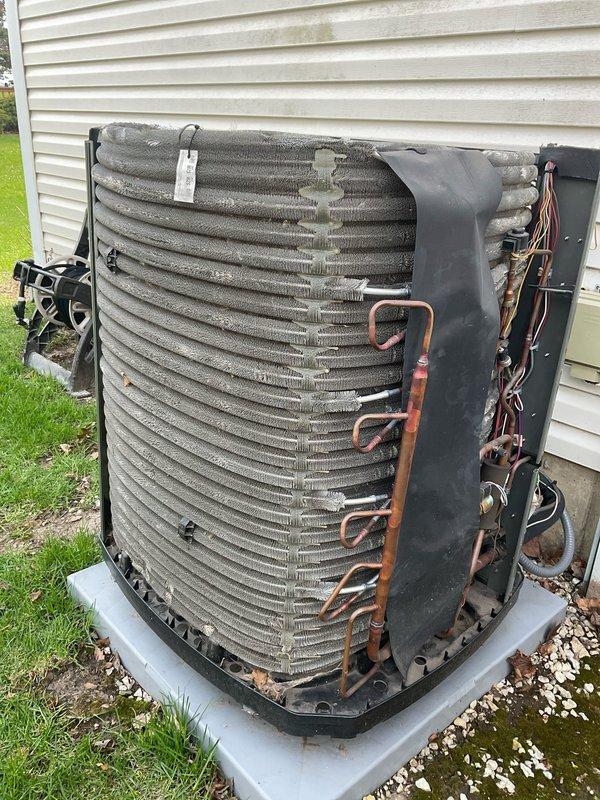 Completed BFMA preventive maintenance tune-up on outdoor air conditioning condenser unit. Removed side panel to access internal components and performed comprehensive inspection of refrigeration system including copper refrigerant lines, U-bend connections, and condenser coil assembly. Inspected condenser coil fins for debris accumulation and outdoor weathering, noting dirt buildup consistent with normal operation. Checked electrical connections and wiring throughout unit. Verified unit positioning on concrete pad with proper drainage via surrounding gravel base. All components found to be operational with routine wear patterns observed on exterior fins and coil assembly.