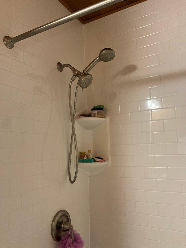 Completed comprehensive plumbing inspection of lower level bathroom and mechanical room. Inspected dual showerhead system with rain head and handheld unit, verified proper operation of brushed nickel fixtures and faucet controls, and confirmed white subway tile surround in good condition with no visible leaks or water damage. Examined water heater, associated copper and PEX supply lines, drainage system, and overhead plumbing connections in utility area, documenting all components with photos for maintenance records.