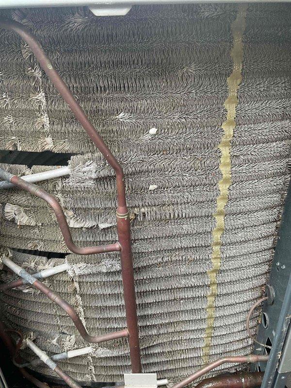 Completed comprehensive A/C tune-up on residential HVAC system. Performed thorough inspection of evaporator coil assembly, noting moderate dust and debris accumulation on fin surfaces with some bent fins visible on left side requiring attention. Inspected copper refrigerant lines and associated piping throughout unit, observing deteriorated insulation wrapping on multiple sections that will need future replacement. Cleaned evaporator coil fins to remove built-up dust and contaminants, improving heat transfer efficiency. Checked all refrigerant line connections for proper sealing and integrity. Noted yellow-tan staining on right edge of coil assembly, likely from moisture or oil residue. Verified system operation and airflow through coil assembly. Recommended monitoring insulation condition on suction lines and scheduling coil deep-cleaning service during next maintenance interval to address remaining buildup in hard-to-reach areas.