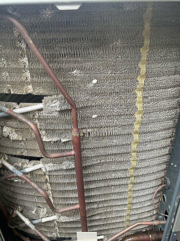 Completed comprehensive A/C tune-up on residential HVAC system. Performed thorough inspection of evaporator coil assembly, noting moderate dust and debris accumulation on fin surfaces with some bent fins visible on left side requiring attention. Inspected copper refrigerant lines and associated piping throughout unit, observing deteriorated insulation wrapping on multiple sections that will need future replacement. Cleaned evaporator coil fins to remove built-up dust and contaminants, improving heat transfer efficiency. Checked all refrigerant line connections for proper sealing and integrity. Noted yellow-tan staining on right edge of coil assembly, likely from moisture or oil residue. Verified system operation and airflow through coil assembly. Recommended monitoring insulation condition on suction lines and scheduling coil deep-cleaning service during next maintenance interval to address remaining buildup in hard-to-reach areas.