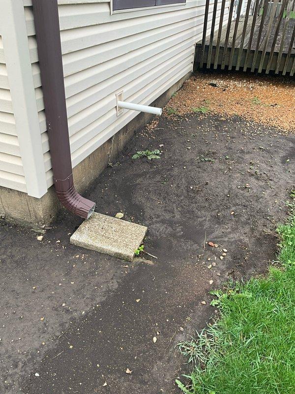 Replaced non-functional sump pump system in residential crawl space. Removed existing failed pump and basin from deteriorated below-grade area showing significant water damage and moisture infiltration on concrete walls. Installed new sump pump with black ribbed basin positioned on gravel floor and connected white PVC discharge line extending vertically through crawl space. Verified discharge pipe properly routes water away from foundation exterior, with horizontal PVC outlet positioned near ground level on building perimeter. System tested and confirmed operational for effective groundwater management and foundation protection.