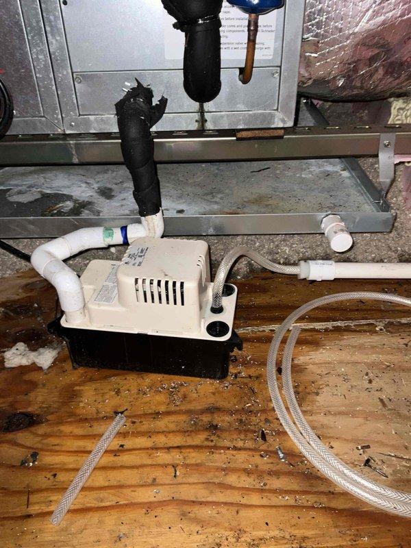 Responded to service call for water leak from attic-mounted air conditioning system causing water intrusion into basement. Upon inspection, found condensate pump experiencing drainage issues with visible water accumulation on wooden platform beneath unit. Identified deteriorated insulation on condensate piping and evidence of ongoing moisture problems around pump assembly. Documented existing conditions including damaged pipe insulation, water staining on plywood surface, and condensate pump installation requiring attention to resolve leak and prevent further water damage.