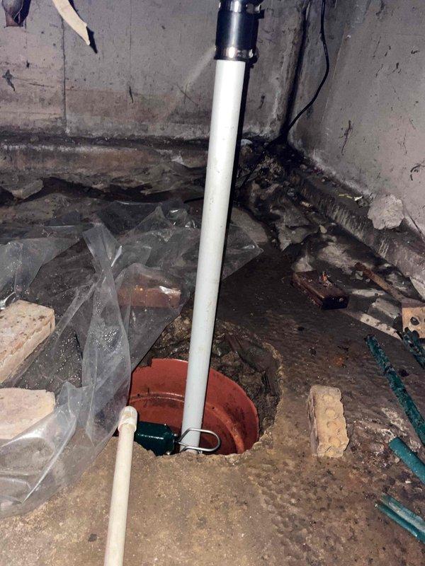 Responded to follow-up service call regarding sump pump system that previously exhibited burning smell near electrical outlet. Electrician had replaced outlet with grounded receptacle based on theory that water discharge was spraying overhead rafters and outlet during pump operation. Conducted comprehensive inspection of sump pump installation, discharge piping, and surrounding area. Examined PVC discharge line configuration and pump positioning within sump pit. Verified proper pump operation and assessed potential water spray issues. Documented existing conditions including deteriorated basement infrastructure, debris accumulation around sump pit area, and discharge pipe routing through overhead space. Confirmed system functionality and identified areas where water discharge pattern could impact nearby electrical components during high-volume pumping cycles.