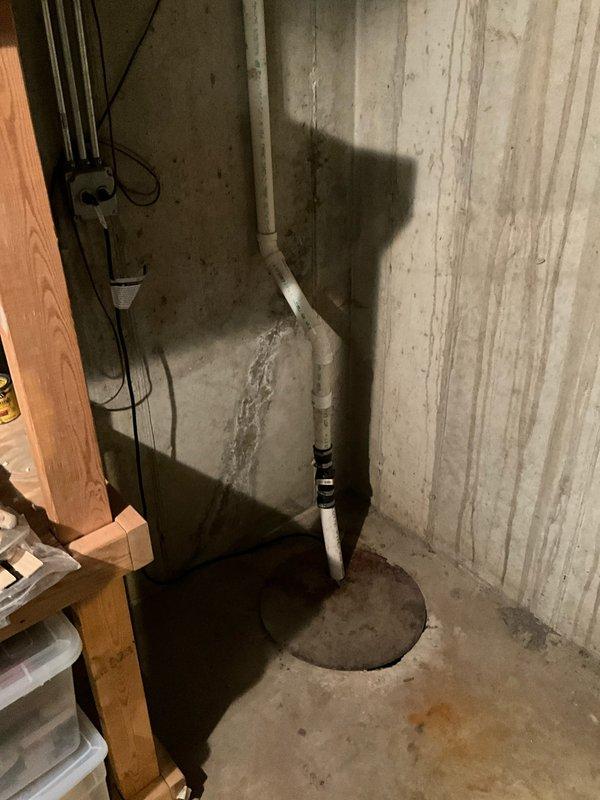 Responded to service call for sump pump issues in residential basement. Upon inspection, assessed sump pump system including discharge piping, electrical connections, and pit condition. Evaluated white PVC discharge line with wall-mounted routing and black coupling adapter at floor penetration point. Inspected electrical junction box and associated wiring serving the pump system. Documented basement moisture conditions including wall staining and efflorescence on concrete surfaces, which indicated previous water intrusion. Photographed existing sump pit configuration and discharge infrastructure for service records.